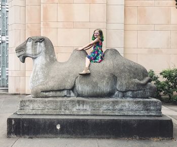 Young woman sitting on statue against wall