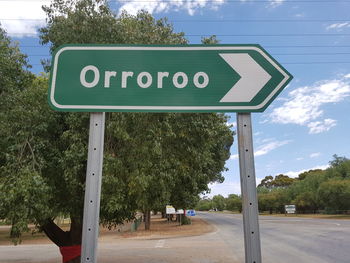 Road sign by trees against sky