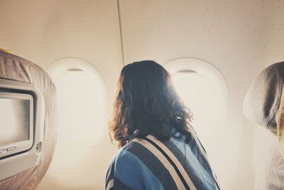 Rear view of woman standing by airplane window