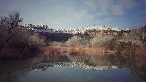 Reflection of trees and town on calm lake against sky