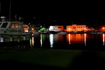 Boats moored in river against illuminated buildings in city at night