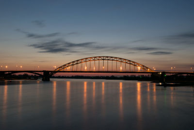 Arch bridge over river against sky at sunset