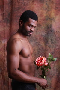 Shirtless young man holding flower while standing against wall