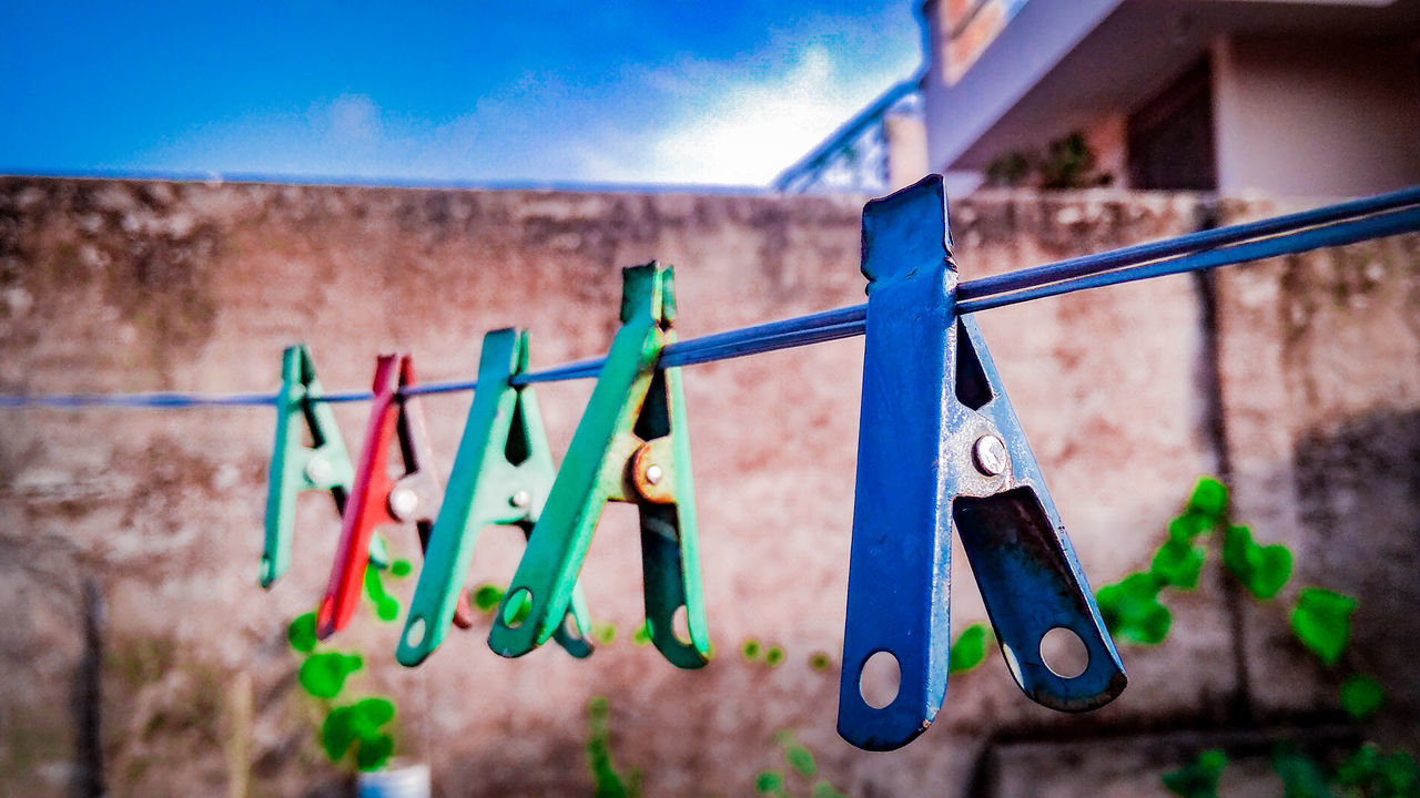 clothesline, clothespin, hanging, laundry, clothing, multi colored, no people, day, focus on foreground, nature, blue, drying, sky, in a row, rope, wall - building feature, wall, close-up, selective focus, outdoors