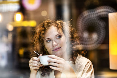 Portrait of smiling young woman with coffee cup behind windowpane of a coffee shop