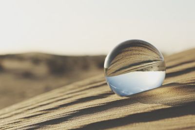 Close-up of crystal ball on beach against clear sky