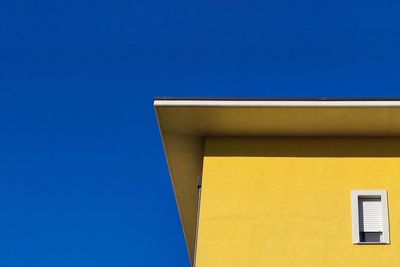 Low angle view of yellow building against clear blue sky