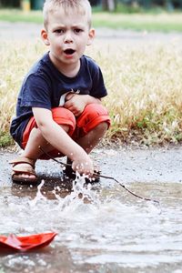 Cute boy looking at paper boat while splashing water at lakeshore