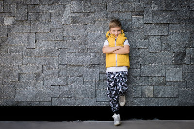 Smiling boy with arms crossed leaning on brick wall and looking at camera. copy space.