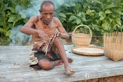 Shirtless senior man making straw basket