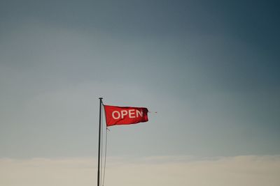 Low angle view of red flag with open text against sky