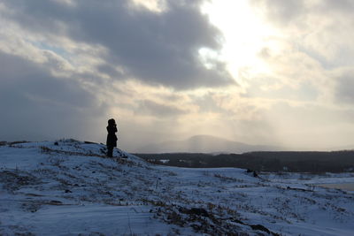 Silhouette woman standing on snow covered field against sky during sunset