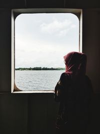 Man sitting by window against sky