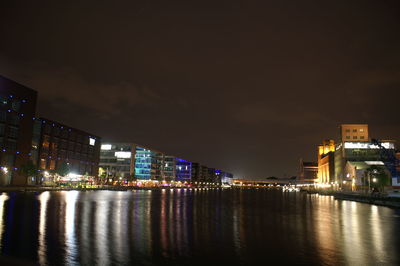 Illuminated buildings by river against sky at night