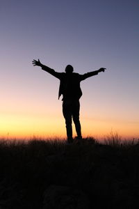 Silhouette man standing with arms outstretched against sky
