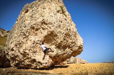 Man climbing rock formation against clear sky