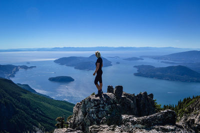 Rear view of woman standing on cliff by sea against clear blue sky