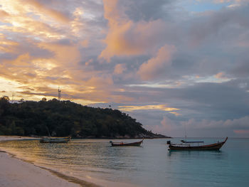 Sailboats moored on sea against sky during sunset