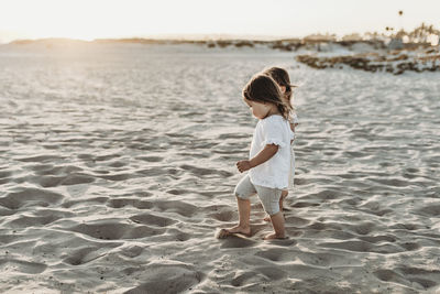 Side view of young toddler girls holding hands and walking at beach