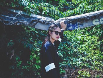 Portrait of young woman wearing sunglasses standing in forest