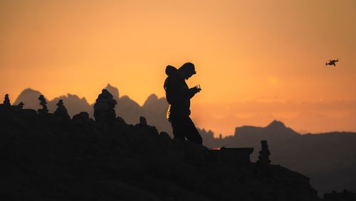 Silhouette man standing on rock against sky during sunset