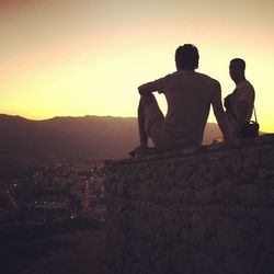 Silhouette men sitting on retaining wall against clear sky