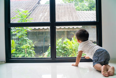 Full length of cute boy crouching by window at home