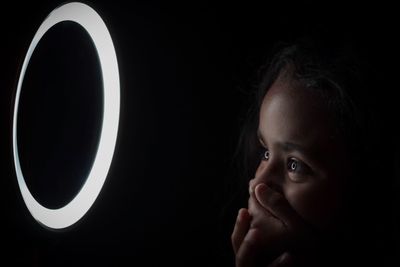 Shocked girl looking at illuminated circle against black background