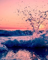 Water splashing in sea against sky during sunset