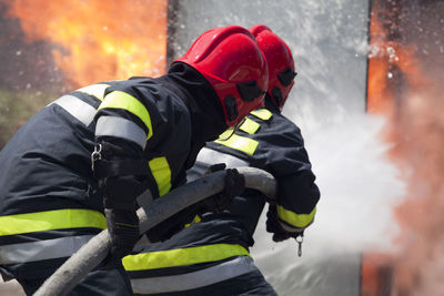 Rear view of firefighters spraying water on fire