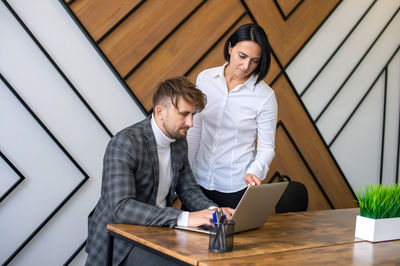 A woman helps a man to do work on a laptop in the office