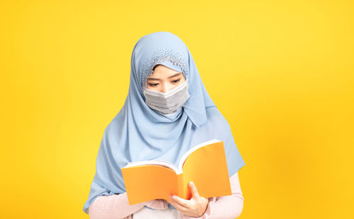 Portrait of teenage girl covering face against yellow background