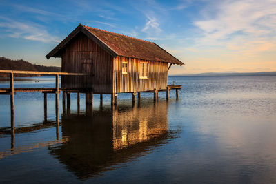 Stilt house by sea against sky during sunset