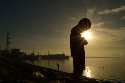 Silhouette man standing by sea against sky during sunset