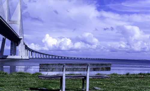 Bench by vasco da gama bridge over tagus river against sky