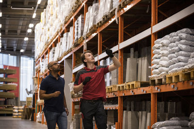 Salesman gesturing and talking with mature customer near rack at hardware store