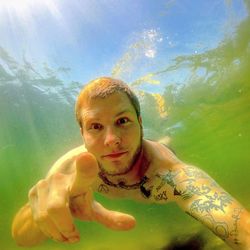 Portrait of tattooed young man gesturing while swimming in sea