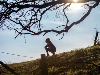 Woman sitting on bare tree against sky