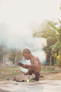 Shirtless senior man making straw basket