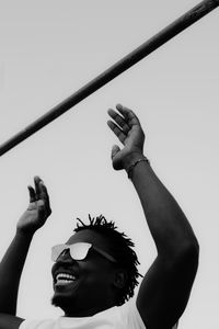 Low angle view of man holding sunglasses against clear sky