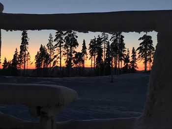 Silhouette trees on snow covered land against sky during sunset