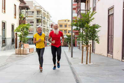 Front view of a happy senior couple running in the city