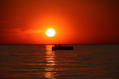 Silhouette boat in sea against orange sky