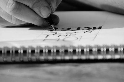 Cropped hand of person holding pen over book with text