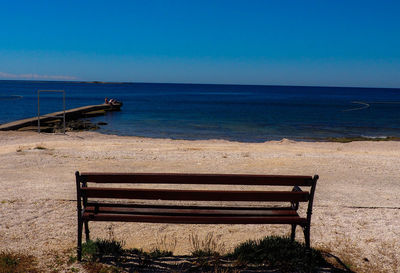 Empty deck chairs on beach against clear blue sky