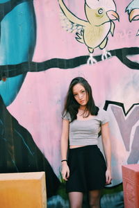 Full length of young woman standing against graffiti