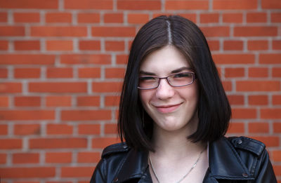 Portrait of a smiling young woman against brick wall
