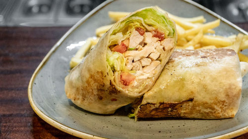 A tasty image of a freshly prepared chicken tortilla wrap filled with salad and served with fries