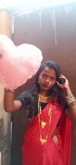 Portrait of smiling young woman holding camera while standing outdoors