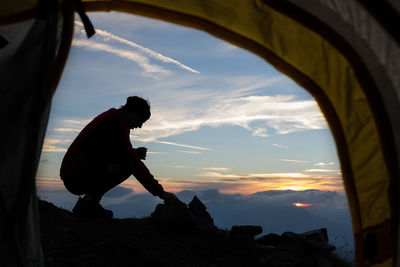 Side view of silhouette man seen through tent against sky during sunset